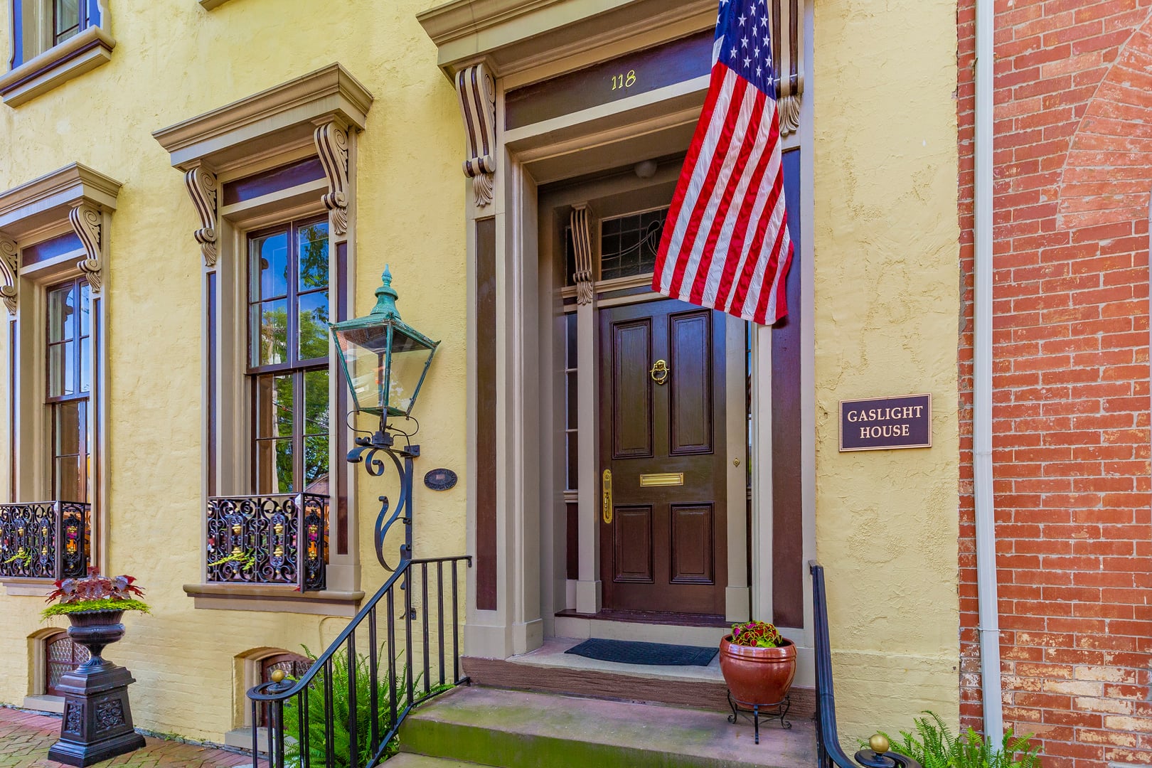 Front entrance of the historic 1810s Gaslight House at 118 East Church Street in Frederick, Maryland, showing a yellow stucco Italianate rowhome with a gas lamp, American flag, and dark wood door
