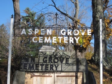 A nineteenth-century New England cemetery on a hillside with a Civil War monument visible above the entrance