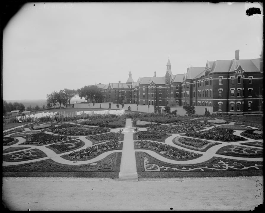 The hospital's formal garden with geometric flower beds in front of the main building, photographed by Frank Cousins