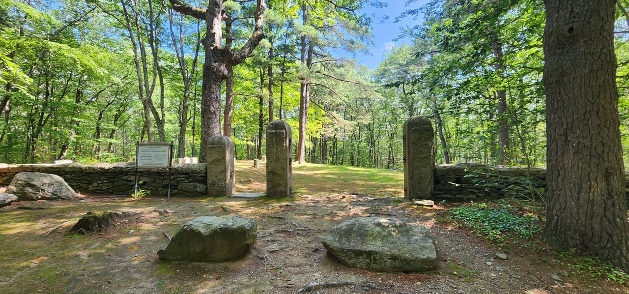 The stone gateposts of the Friends (Quaker) Cemetery entrance in Leicester, Massachusetts, with the ornate iron 'spider' gate visible between them.