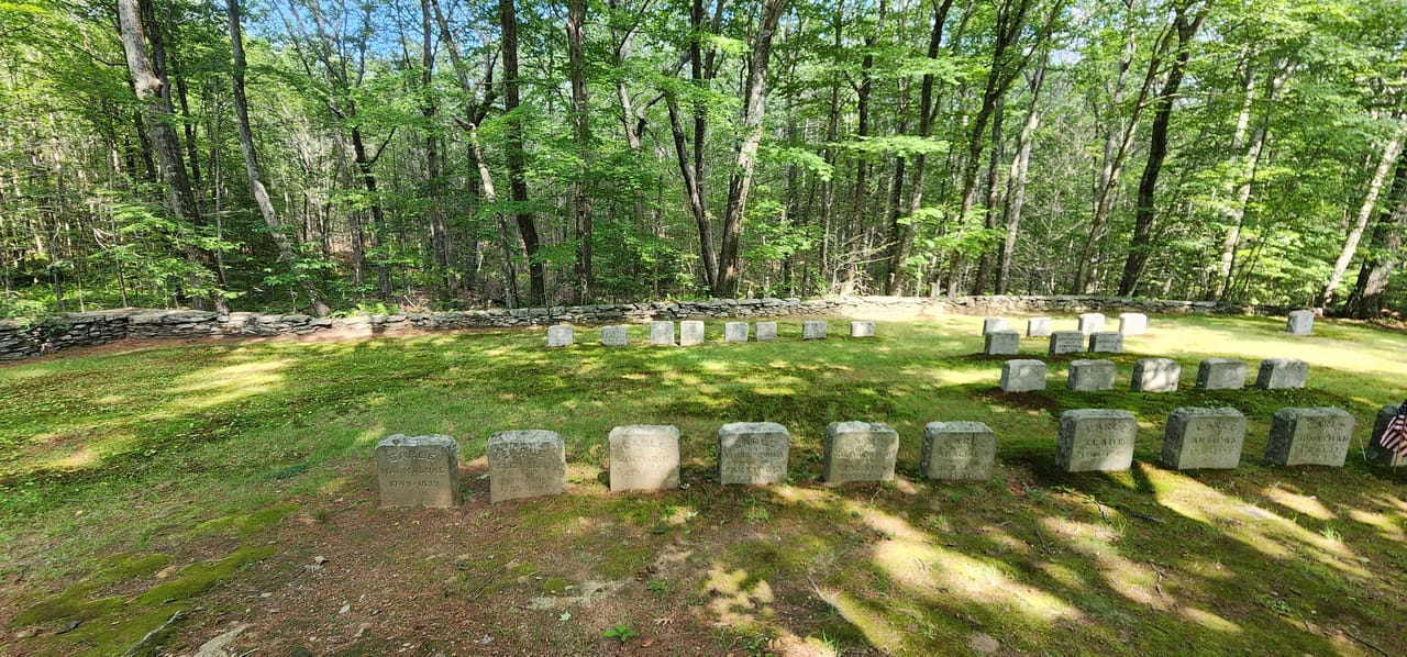 A wooded row of weathered granite headstones inside the Quaker Cemetery, bordered by a dry-stone wall.