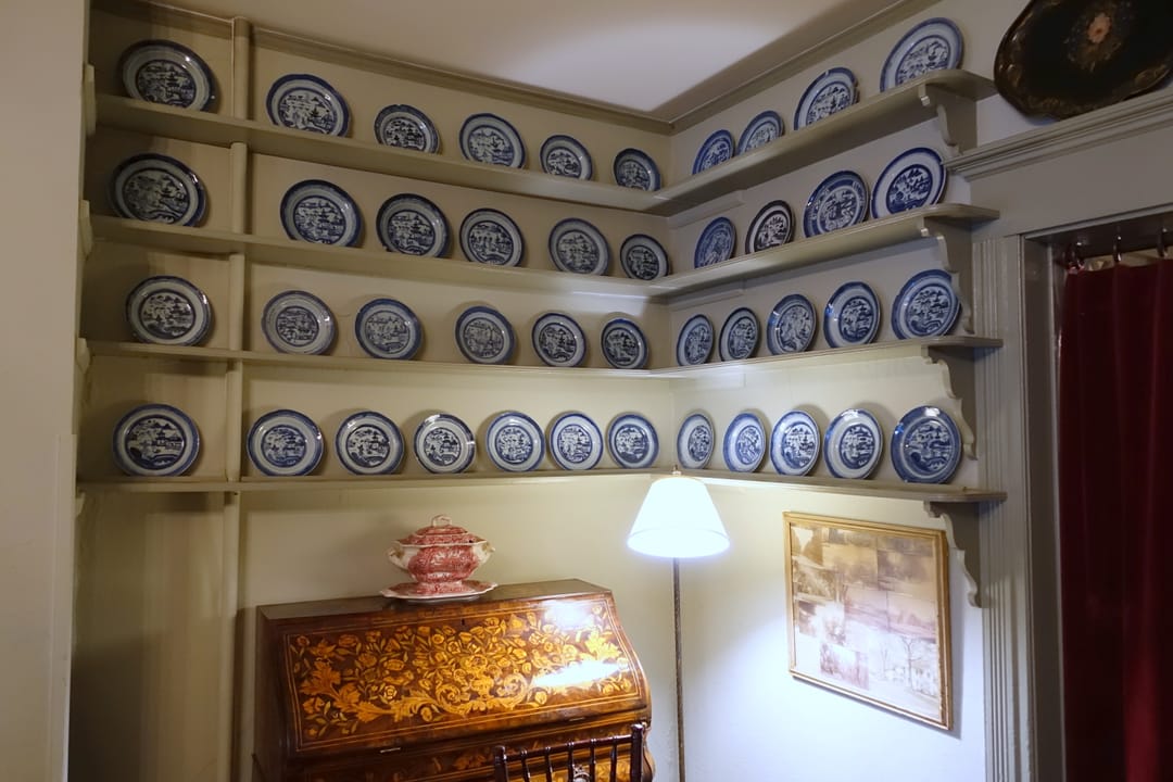 Blue-and-white china plates displayed on corner shelves above an inlaid writing desk in a Red Lion Inn dining room, Stockbridge, Massachusetts, 2017.