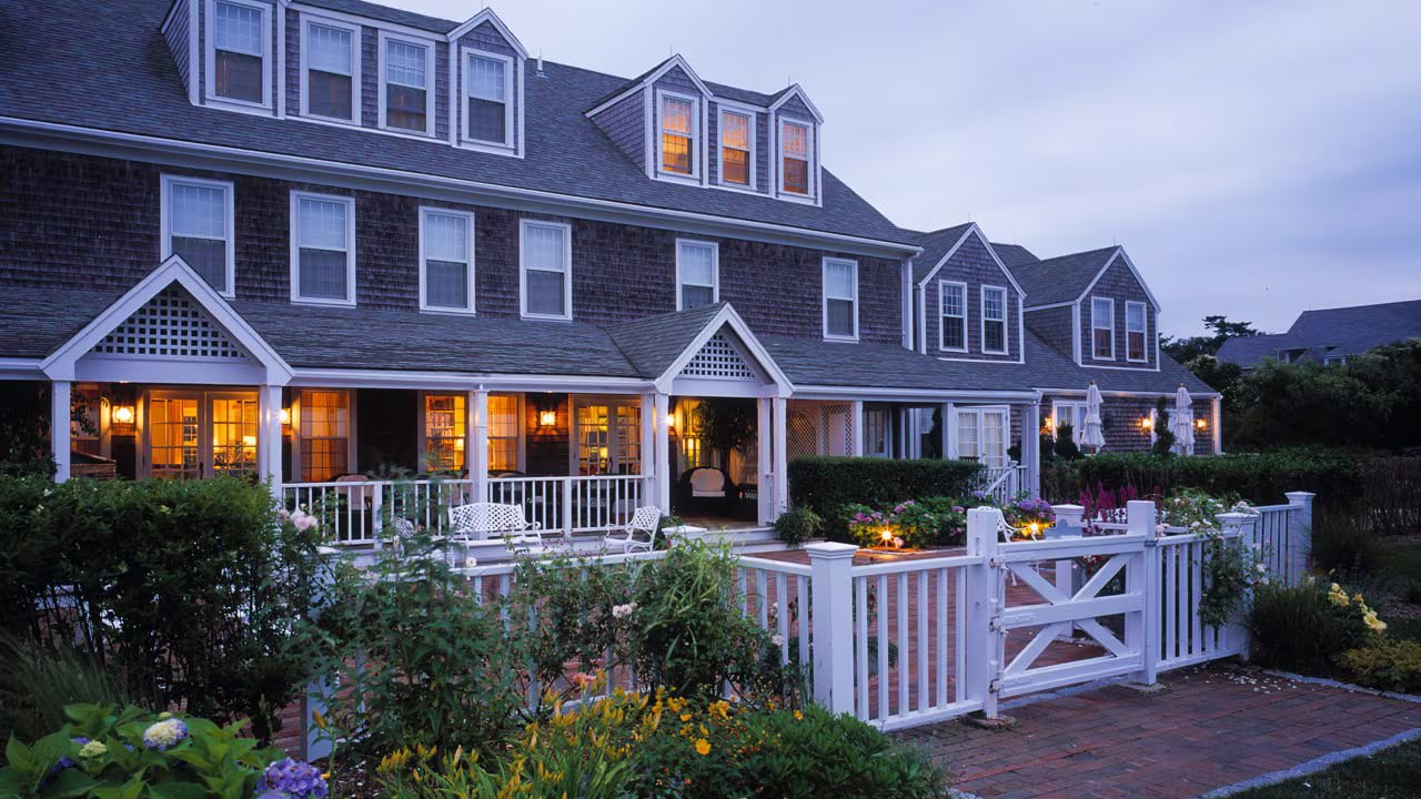 The Wauwinet inn at dusk on Nantucket, its gray-shingled New England facade with white porch railings and cottage gardens