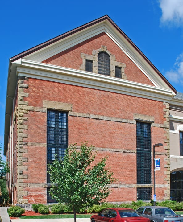 A brick former cell-block building with a pedimented gable and barred windows, part of the old prison complex, Jackson, Michigan.