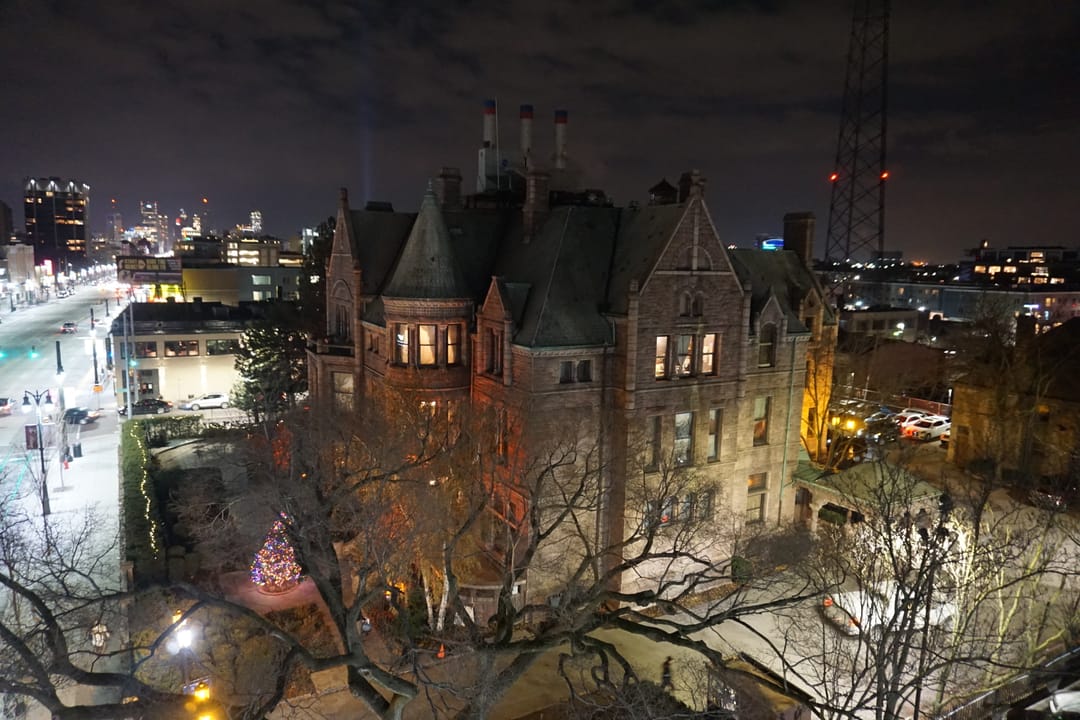 The David Whitney House lit up at night, viewed from above with the Detroit skyline behind it, December 2018.