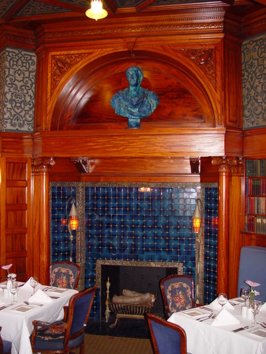 A carved wood and blue-tile fireplace with a bronze bust in one of the David Whitney House's dining rooms, set for service.