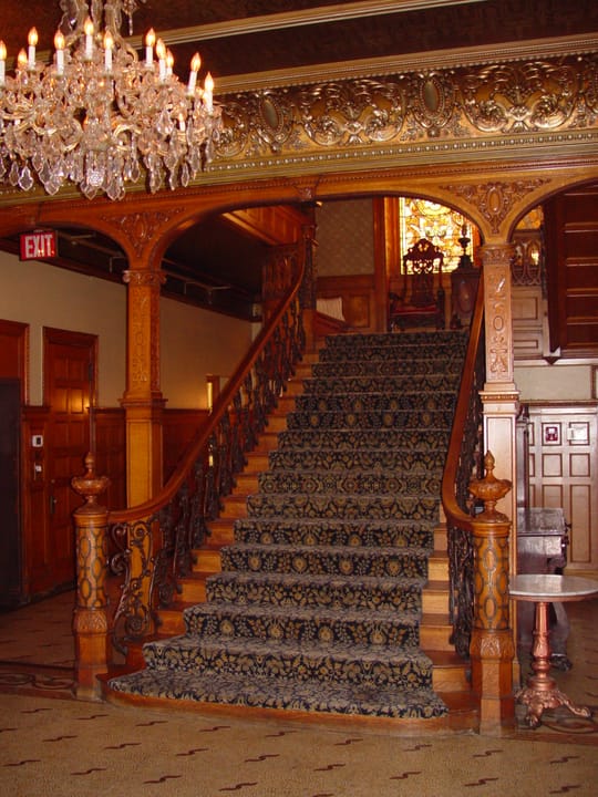 The carved wood grand staircase and crystal chandelier inside the David Whitney House.