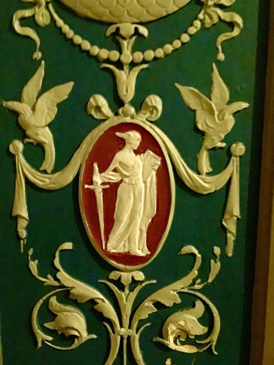 A painted plaster relief panel inside the auditorium, green and gold with a classical robed figure, part of the building's original 1920s ornamentation.