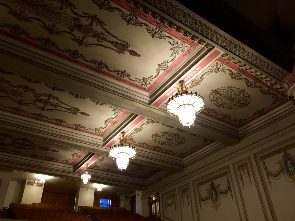 The auditorium's painted and gilded ceiling with hanging glass chandeliers, viewed from the rear of the hall toward the balcony.