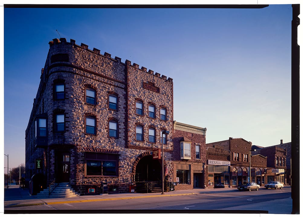 The Calumet Hotel's rock-faced quartzite corner tower with battlements and arched corner entrance, beside neighboring Main Street storefronts, Pipestone, Minnesota, in a Historic American Buildings Survey color photograph by Jet Lowe.