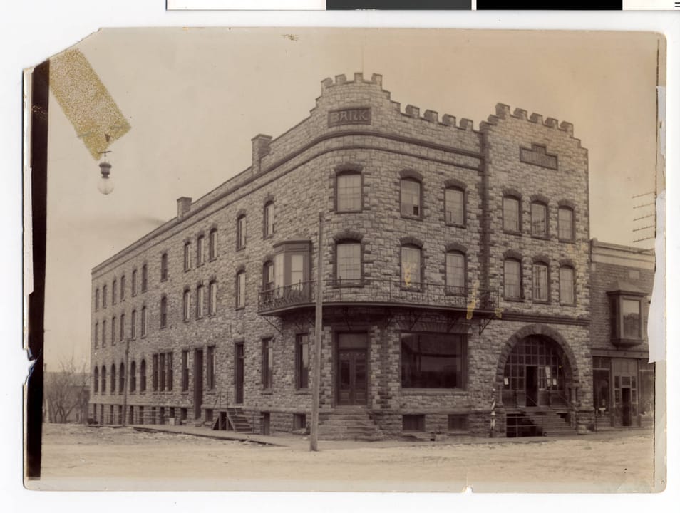 The Calumet Hotel, a quartzite building with a crenellated corner tower, arched corner entrance and corner bay window, seen from the northeast, Pipestone, Minnesota, in a photograph from about 1900 to 1904.