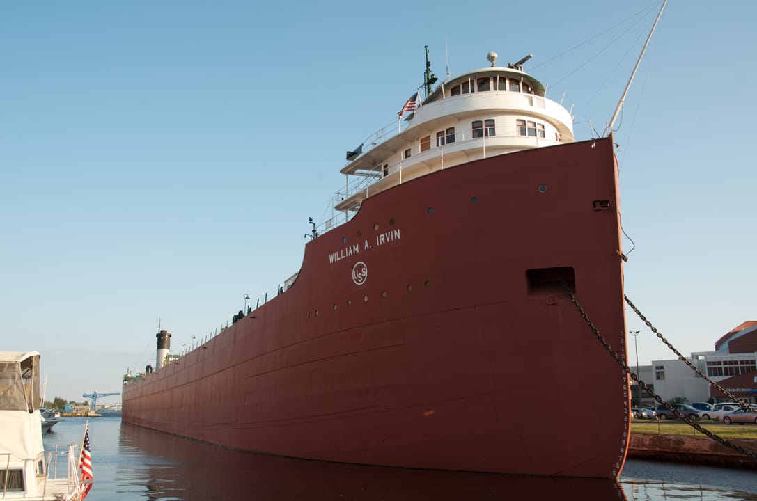 The SS William A. Irvin viewed from the northwest at its Minnesota Slip berth in Duluth Harbor, full red hull and white pilothouse against a clear sky.