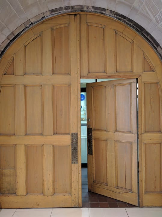 The mansion's heavy carved wooden entrance doors, open, photographed inside the museum's public visitor entrance.