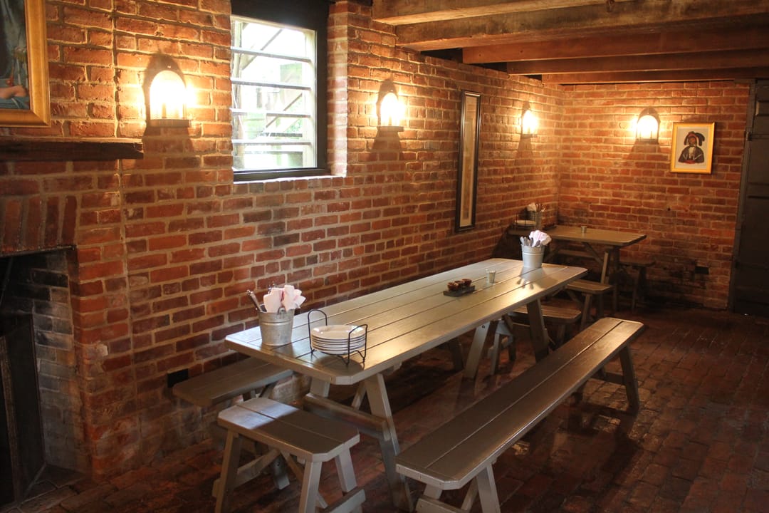 Interior dining room of King's Tavern, exposed brick walls, wall sconces, and a long wooden communal table and benches.