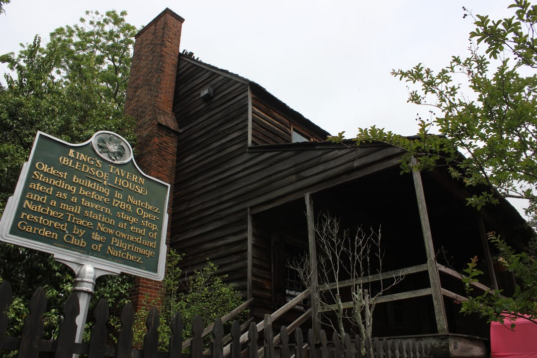 Angled view of King's Tavern's rear/side elevation with the Pilgrimage Garden Club historic marker ('King's Tavern (Blenno House)... Oldest building in Natchez') in the foreground.