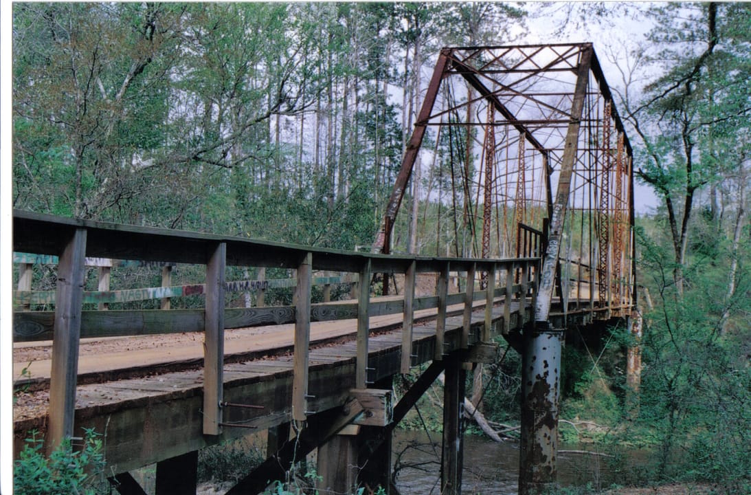 Stuckey's Bridge viewed along its wooden-railed walkway, with the iron truss spans receding into the trees.