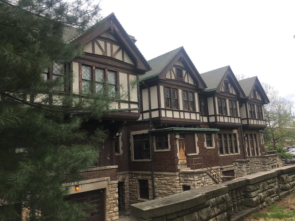 Row of Tudor-style half-timbered gables and leaded windows along Epperson House's wing, with the stone retaining wall below.