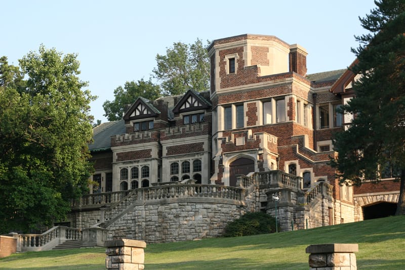 Epperson House seen from the formal stone terrace and balustrade on the UMKC campus, warm-light exterior view showing the tower, gables and grand staircase.