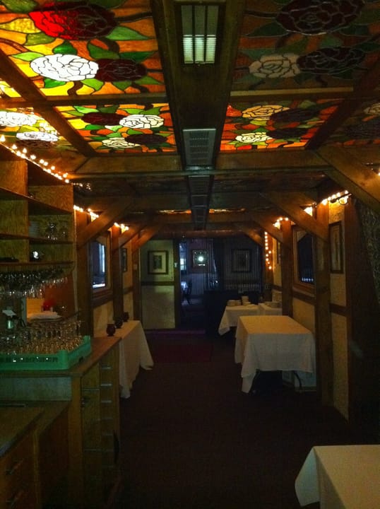 A covered bar corridor inside the Lemp Mansion with a stained-glass rose ceiling, set with tables for service.