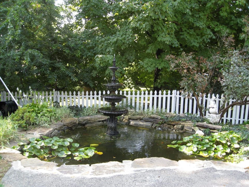 The courtyard fountain and lily pond in the Lemp Mansion's grounds, behind a white picket fence.
