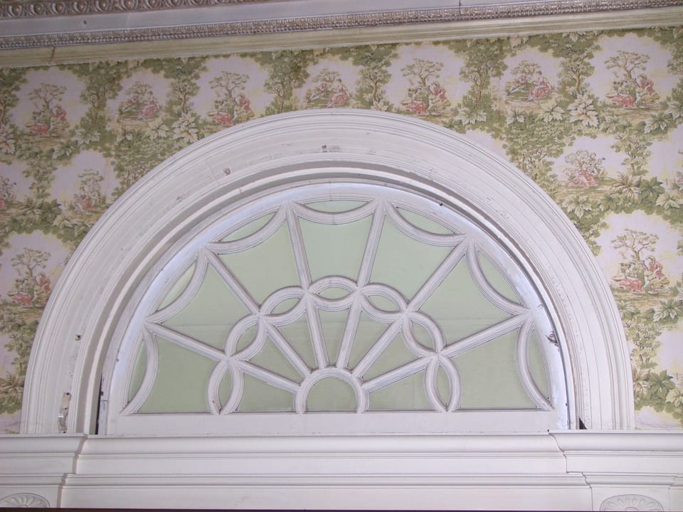 A leaded-glass arched transom above a doorway inside Rockcliffe Mansion, against floral wallpaper.