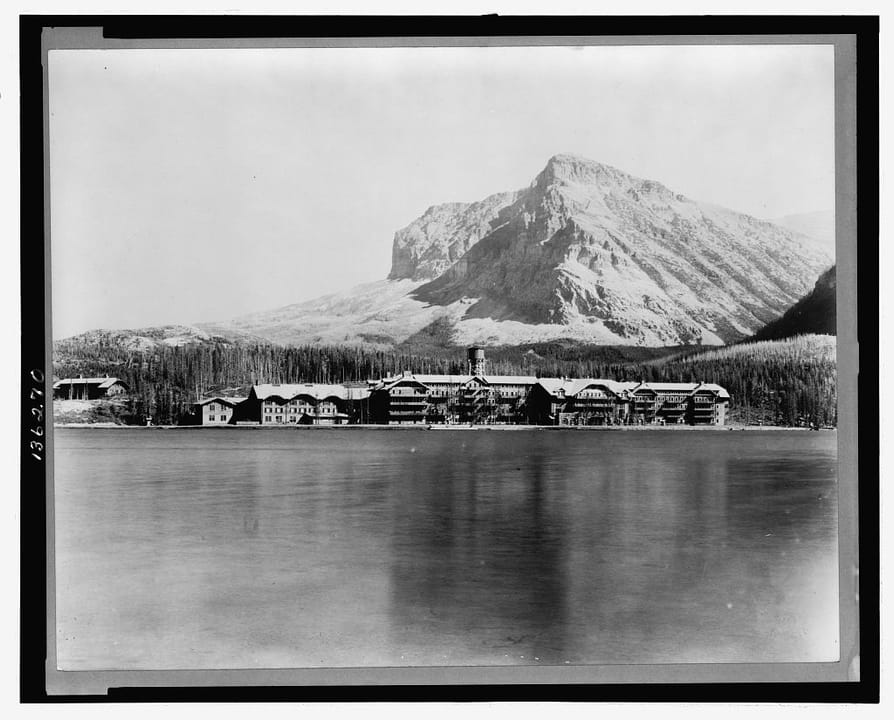 Many Glacier Hotel seen across Swiftcurrent Lake with Grinnell Point behind it, published by the Kiser Photo Co., c. 1921.
