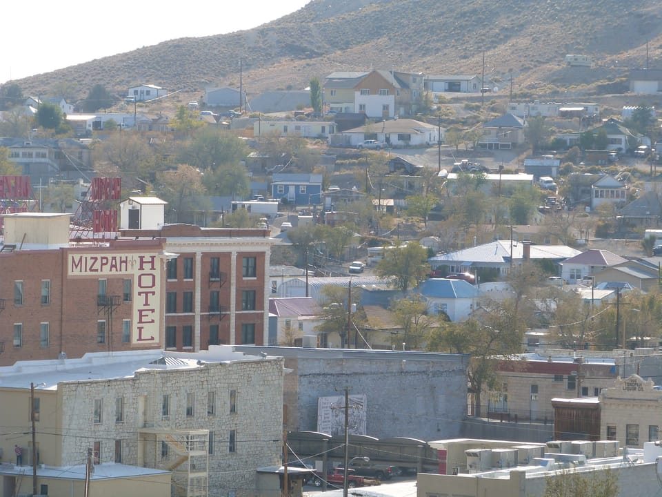 Elevated hillside view of downtown Tonopah with the Mizpah Hotel's tan facade and rooftop sign standing out among the surrounding lower buildings -- an establishing shot of the hotel in its mining-town setting.