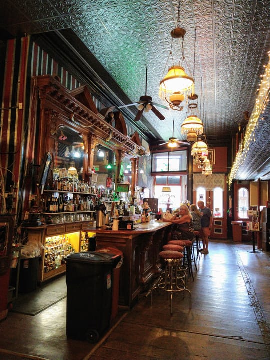 The long bar room at the Silver Queen Hotel, Virginia City, with its pressed-tin ceiling, hanging lamps and carved back bar, August 2021.