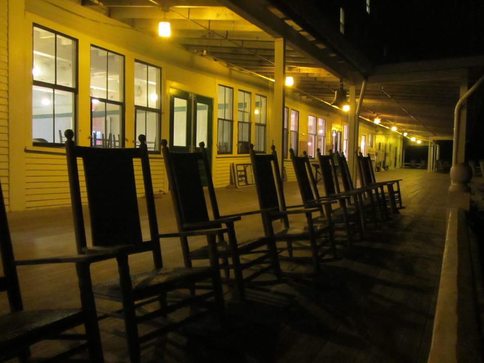 The Oceanic Hotel's long porch lit at dusk, its rocking chairs lined up along the row of windows, Star Island, New Hampshire.
