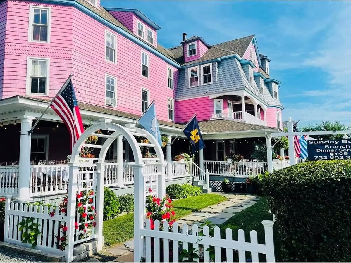 Exterior of The Grenville Hotel and Restaurant in Bay Head NJ, a pink Victorian shore hotel with American flag and white picket fence.