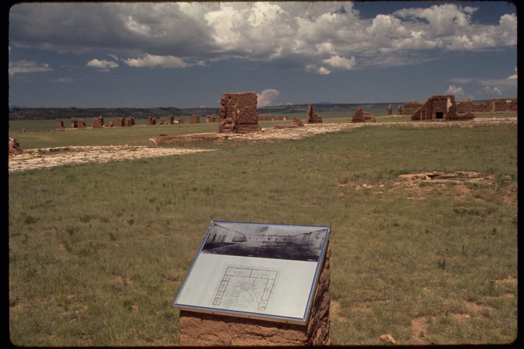 Fort Union's adobe ruins with a wayside exhibit panel in the foreground, under a stormy sky, Fort Union National Monument, New Mexico.