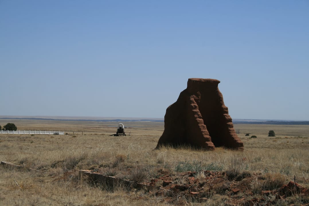 A standing adobe chimney stack ruin at Fort Union, with an interpretive sign and a distant prairie-schooner wagon replica in the background, Fort Union National Monument, New Mexico.