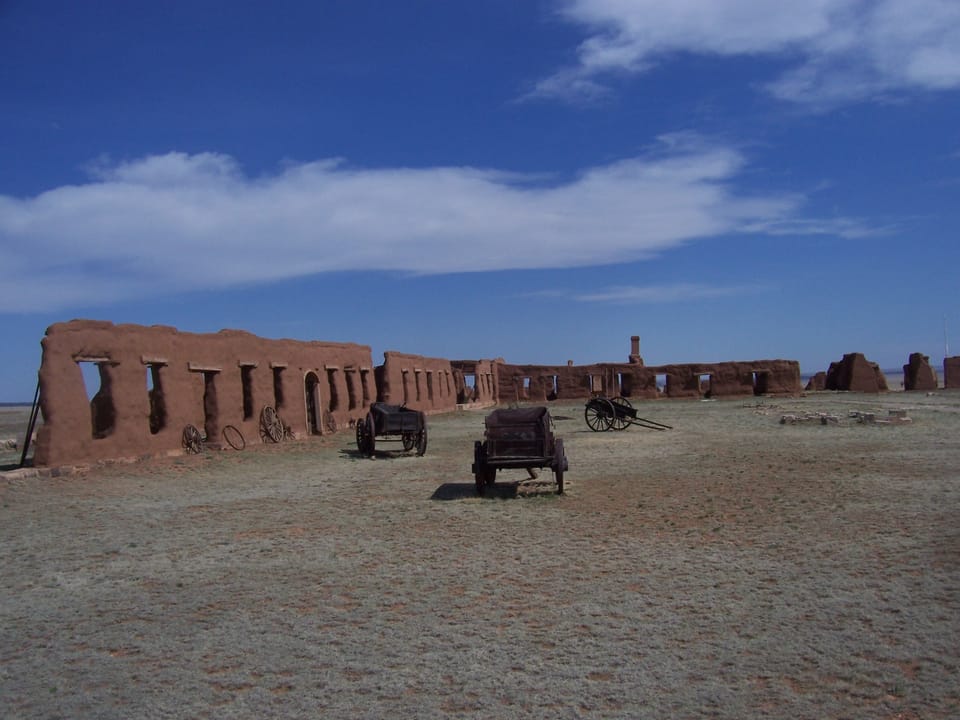 Fort Union's long barracks ruin wall with two restored wagons parked on the parade ground, Fort Union National Monument, New Mexico.