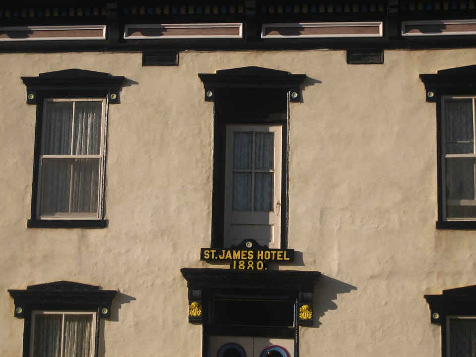 Architectural detail of the St. James Hotel's second-story facade, bracketed cornice, and a datestone/signboard reading 'ST. JAMES HOTEL 1880'.