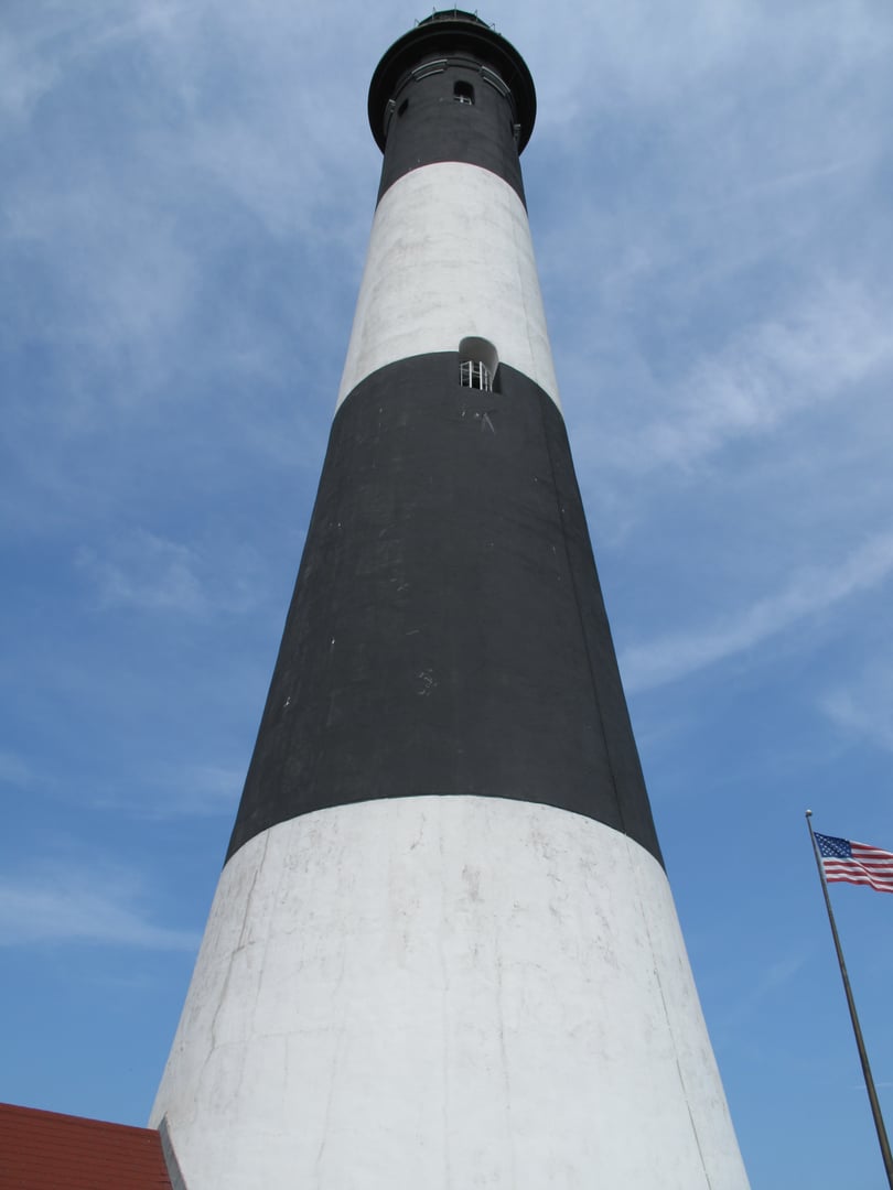 The 168-foot black-and-white-banded Fire Island Lighthouse tower rising above the barrier island dunes on Long Island, New York.