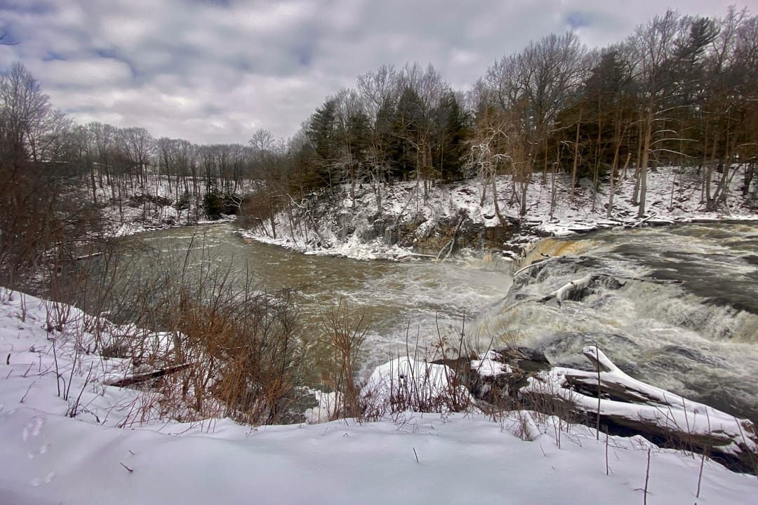 A view of Indian Falls, as seen in January 2023 from the parking lot of the Indian Falls Log Cabin Restaurant in the town of Pembroke, New York (the only publicly accessible view of the falls from land). Locally renowned as a fishing spot, this 20-foot curtain cascade is located at the point where T