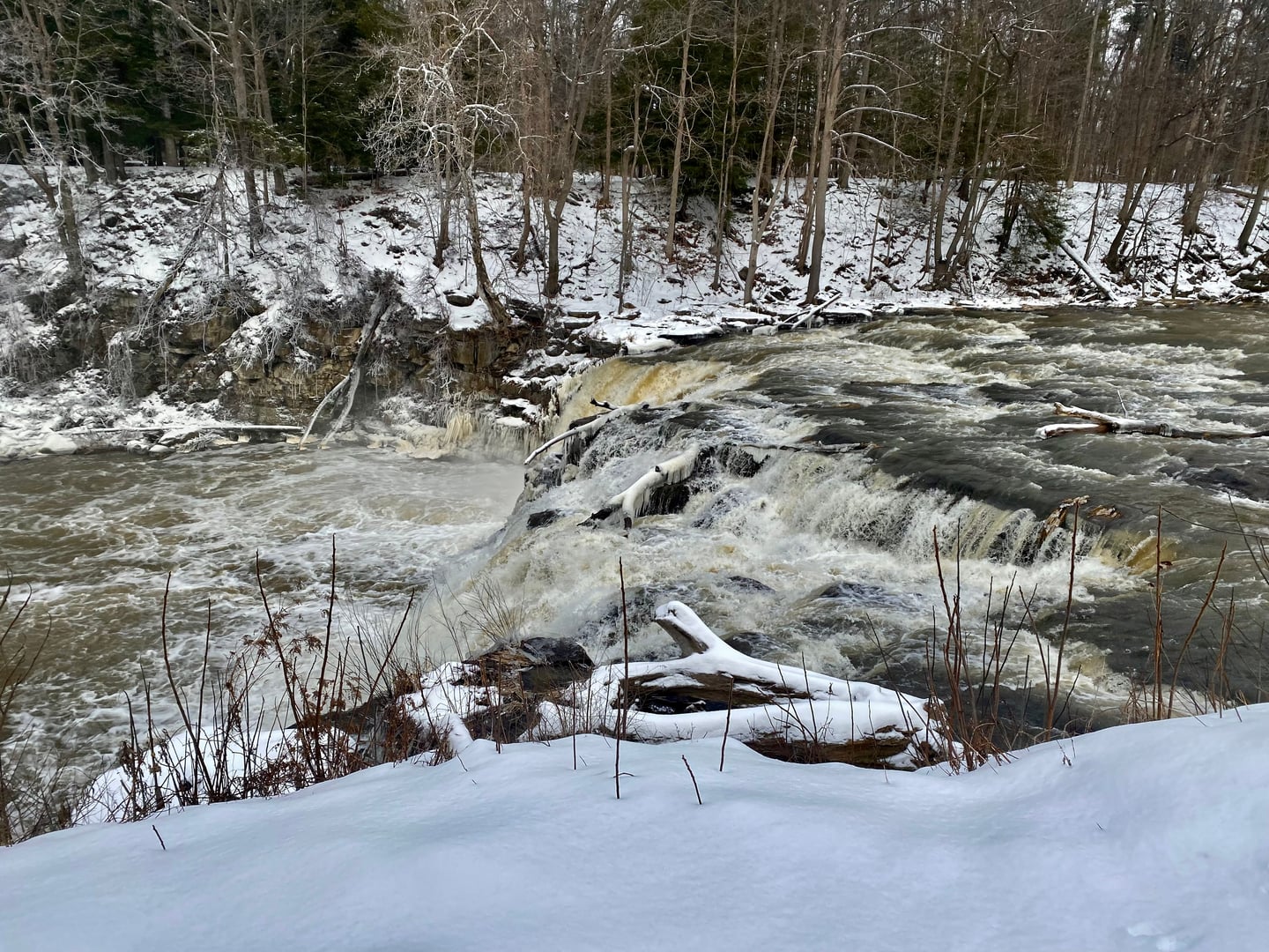 A view of Indian Falls, as seen in January 2023 from the parking lot of the Indian Falls Log Cabin Restaurant in the town of Pembroke, New York (the only publicly accessible view of the falls from land). Locally renowned as a fishing spot, this 20-foot curtain cascade is located at the point where T