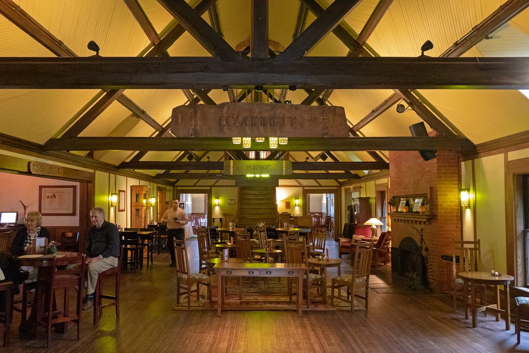The timber-framed lobby bar inside the Roycroft Inn, with guests seated at tables beneath the exposed Arts and Crafts roof trusses, East Aurora, New York.