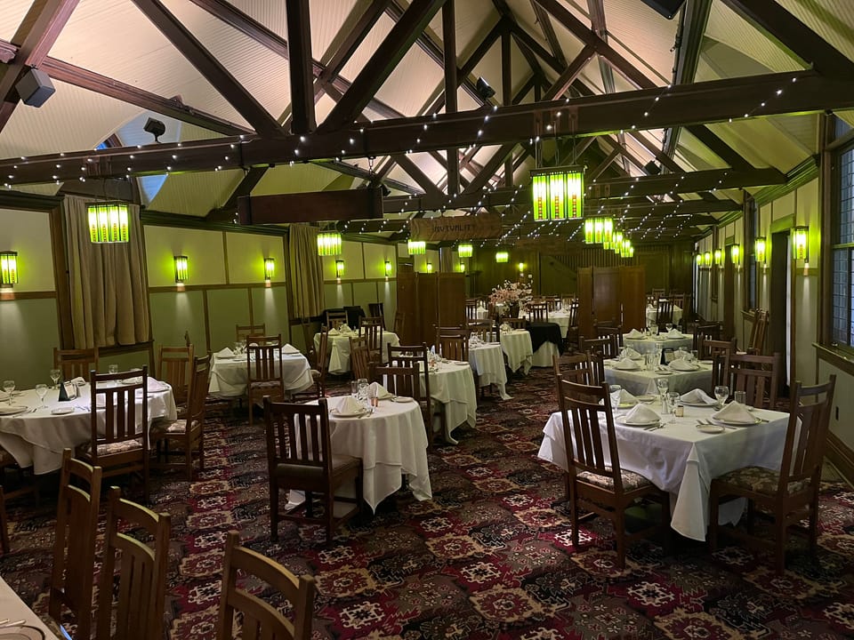 Wide view of the Roycroft Inn's beamed dining hall, with green Arts and Crafts stained-glass pendant lights hanging over tables set for service, East Aurora, New York.