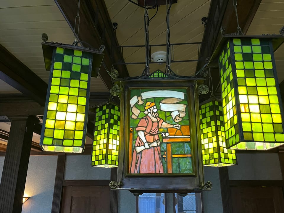 Close-up of a green checkerboard-paned Arts and Crafts stained-glass pendant lamp hanging from the dining hall's timber trusses at the Roycroft Inn, East Aurora, New York.