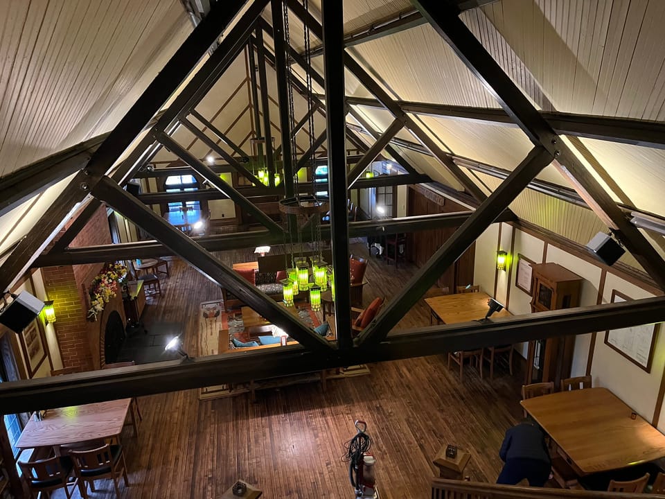 Elevated mezzanine view of the Roycroft Inn's exposed timber roof trusses looking down into the lounge and dining hall below, East Aurora, New York.