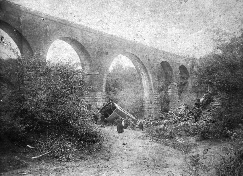 The stone arches of Bostian Bridge over Third Creek near Statesville, North Carolina, photographed from the creek bed after the August 27, 1891 train wreck, with an overturned passenger car at the base of a pier.