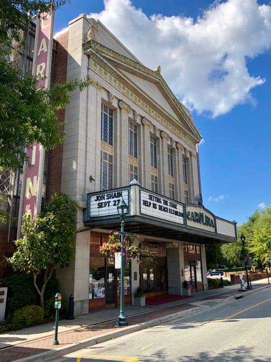 Diagonal street-corner view of the Carolina Theatre's full facade, from the vertical ARCOLINA wall sign down to the marquee and sidewalk entrance, Greensboro, North Carolina.