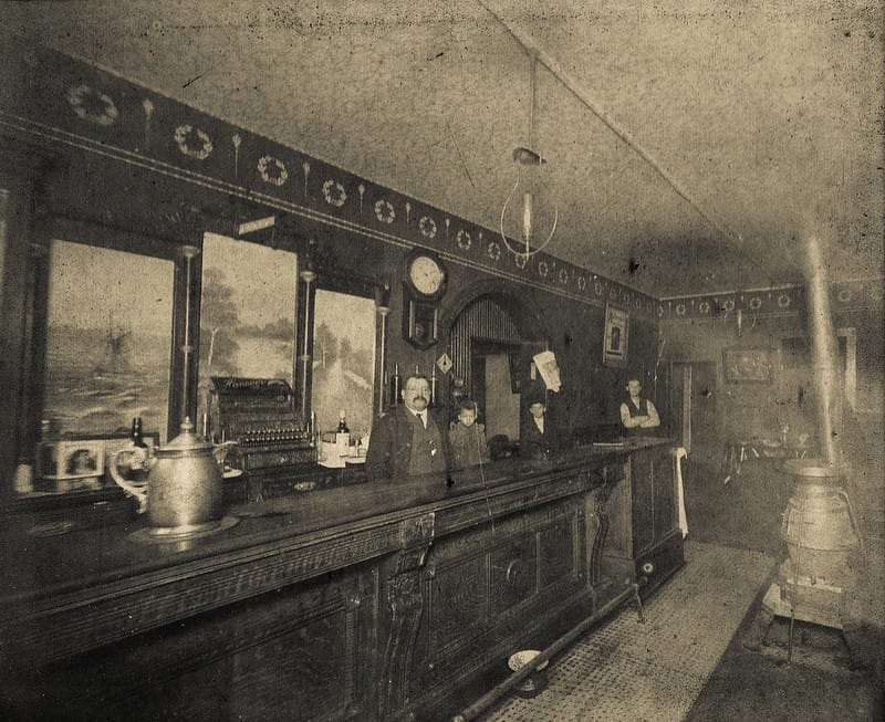 A historic photograph of the bar inside Arnold's, with staff posed behind the counter, taken around the turn of the 20th century.