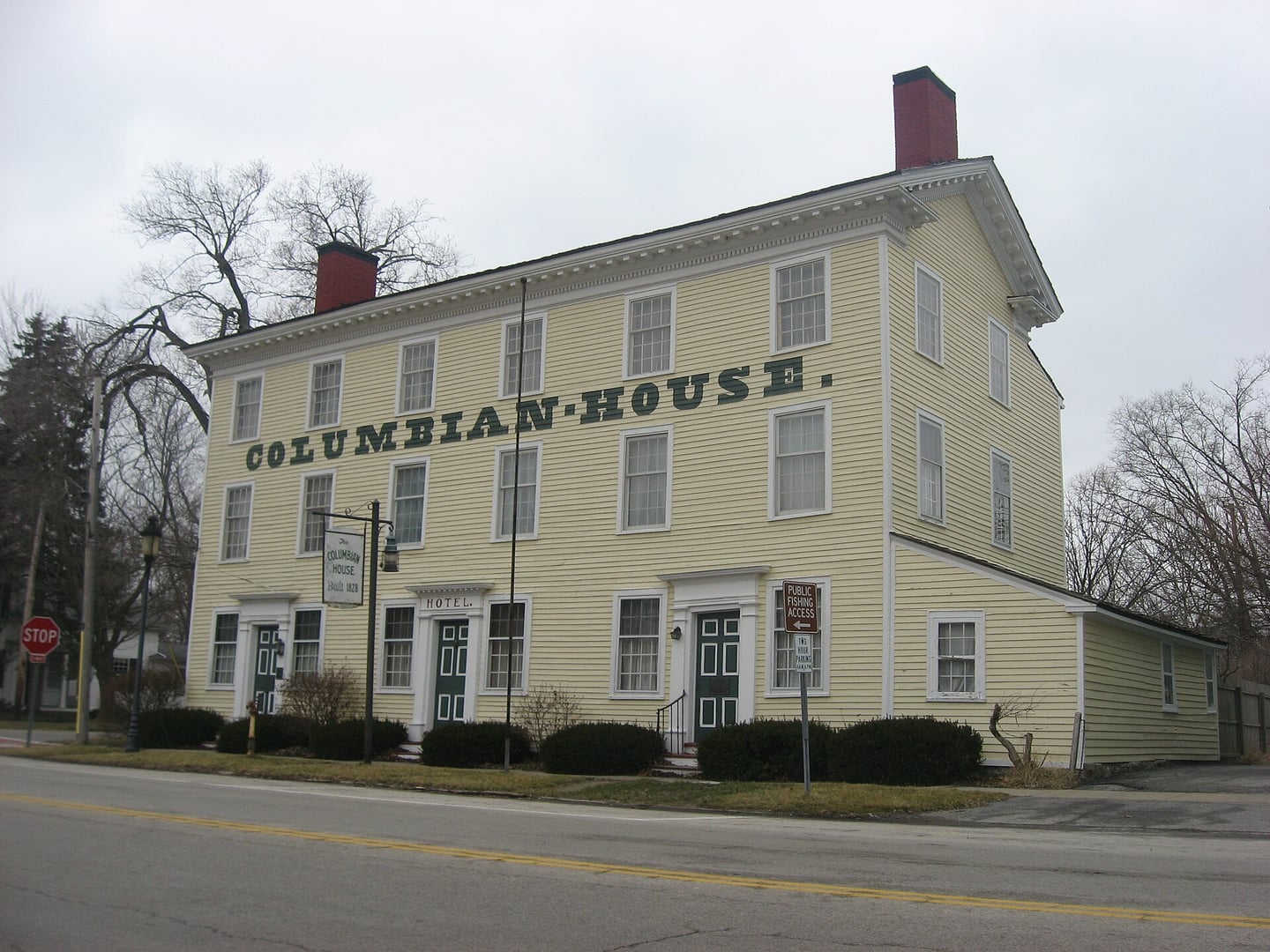 Front and northern side of the bright yellow three-story Columbian House at the corner of River and Farnsworth Roads in Waterville, Ohio