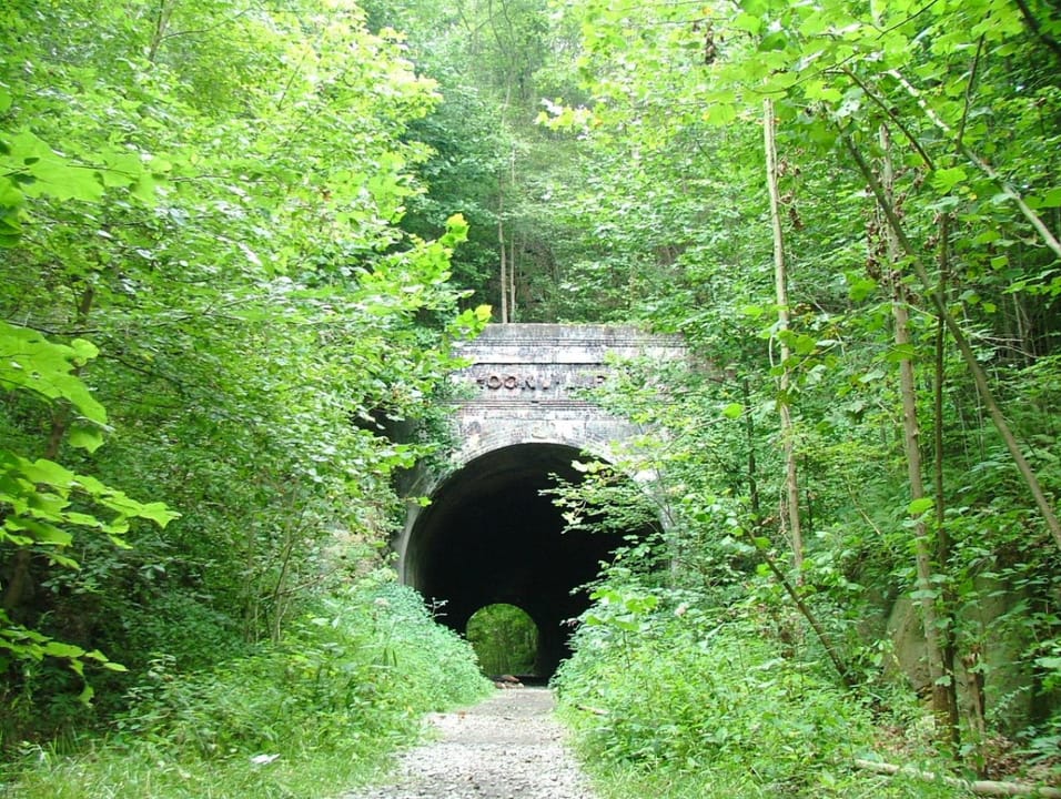 The lettered brick portal of Moonville Tunnel seen from the gravel Moonville Rail-Trail through summer foliage, July 2006.