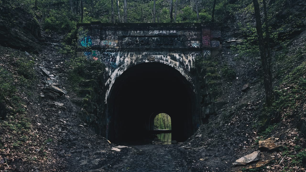 The front of a Moonville Tunnel portal on the Moonville Rail-Trail, with the brick name panel above the arch and the far end of the bore visible, spring 2020.