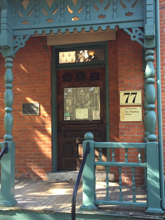 The teal-trimmed front porch and door of the Thurber House, with the "77" street number and "The Thurber House" plaques mounted on the brick.