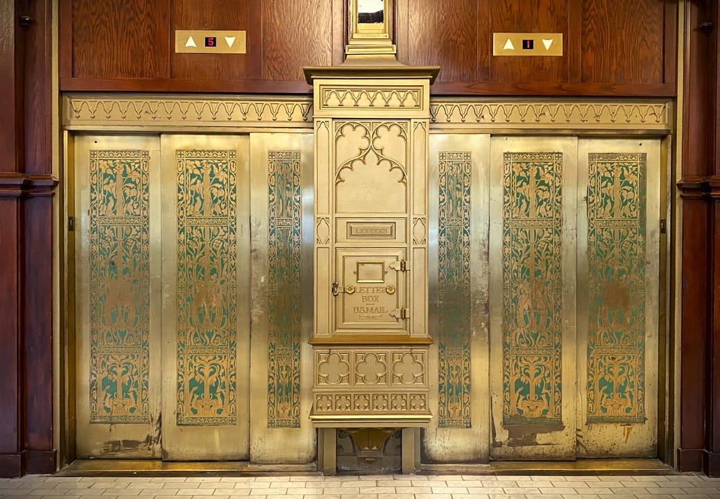 The ornate brass and wood elevator bank in the Skirvin Hilton's lobby, with its original mailbox at center.