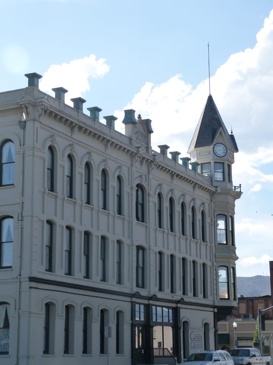 Upward angle on the Geiser Grand Hotel's side facade and corner spire against a cloudy sky, Baker City, Oregon, 2016.